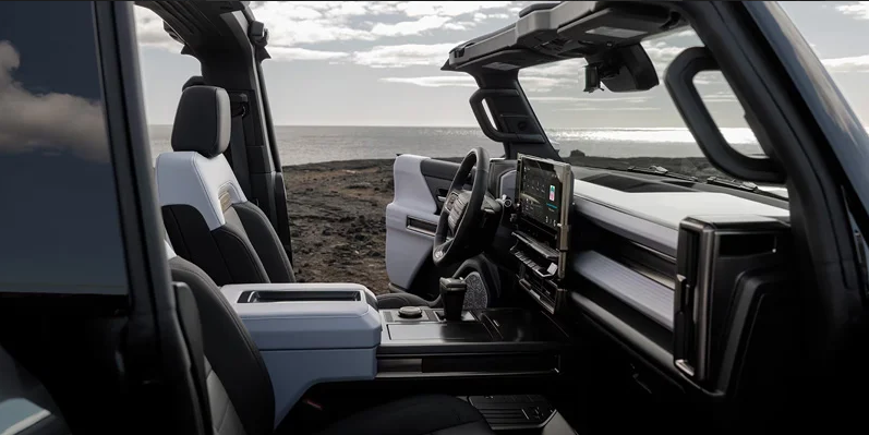 A photo from the passenger side of a 2025 GMC HUMMER EV SUV parked on the beach with the drivers side door open.
