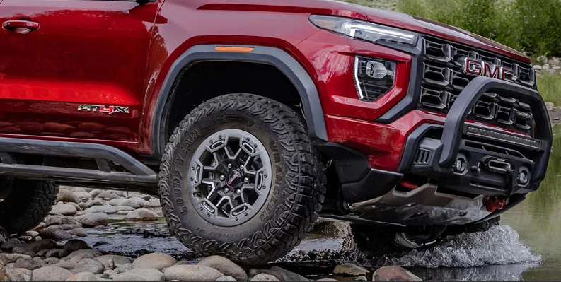 A red 2026 GMC Canyon off-roading through a stream of water.